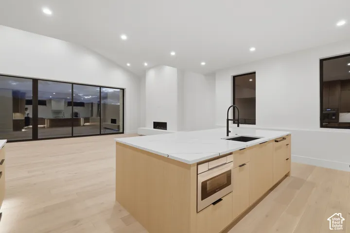 Kitchen island featuring light-finish wood cabinetry, a light-toned countertop, a built-in microwave, and a black faucet, complemented by wood-finish flooring, recessed lighting, and a linear fireplace