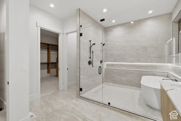Walk-in shower with floor-to-ceiling tile, freestanding soaking tub, recessed lighting, and wall-mounted vanity with built-in storage