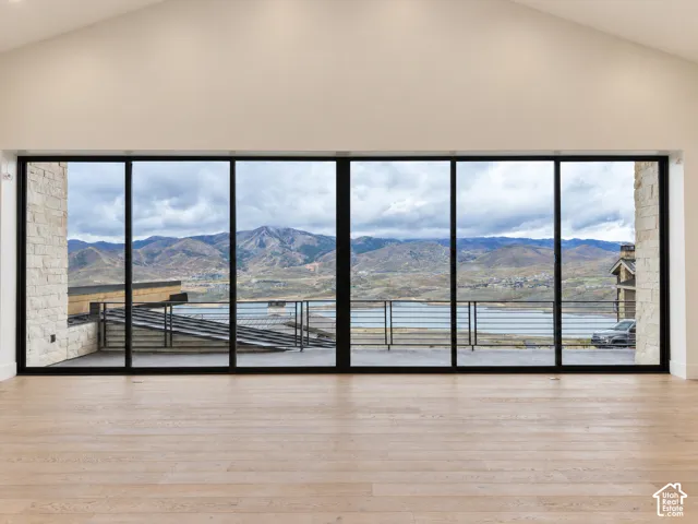 Expansive full-height windows, vaulted ceiling, light wood-finish flooring, and a stone-clad exterior wall section