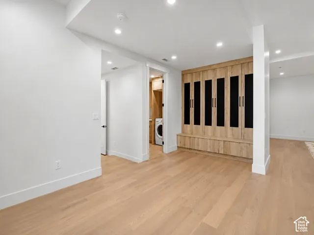 Wood-finish flooring, recessed lighting, built-in storage cabinetry, and a laundry area with a stackable washer