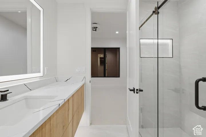 Floating vanity with wood-finish cabinetry, countertop with vein detailing, integrated rectangular sink, wall-mounted backlit mirror, and glass-enclosed shower with tiled walls and built-in shelving