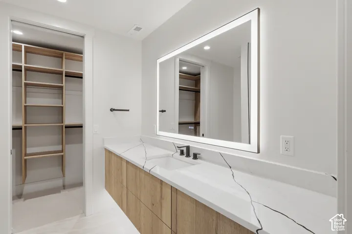 Floating vanity with wood-finish cabinetry, white countertop featuring prominent veining, integrated rectangular sink, matte black widespread faucet, and large rectangular LED-backlit mirror