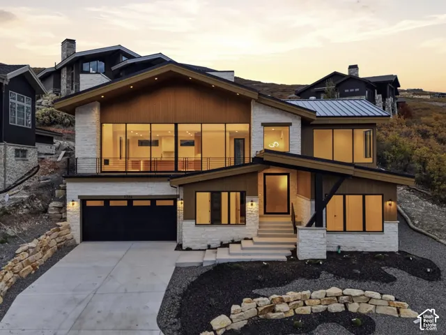 Modern mountain exterior featuring stone masonry, wood-finish siding, floor-to-ceiling windows, metal roofing, and a tiered concrete staircase