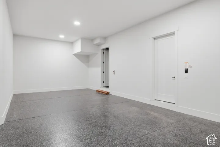Finished garage space featuring epoxy-coated flooring, smooth white walls, recessed ceiling lighting, and a solid-core swing door