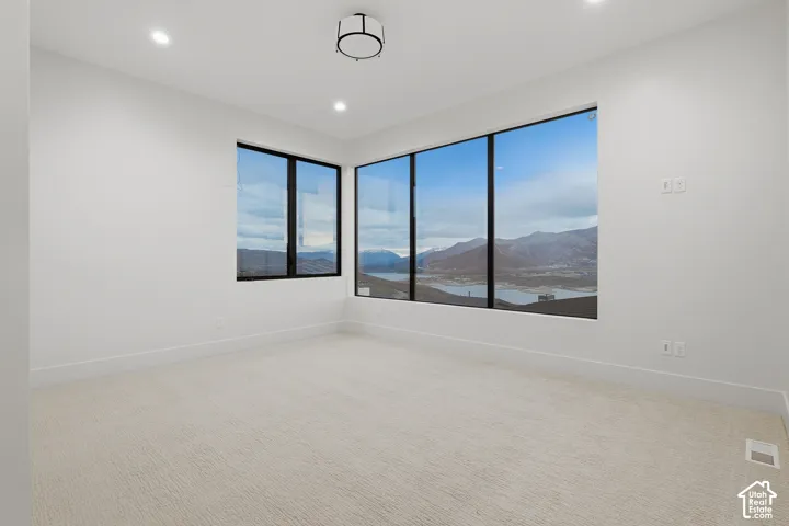 Corner-window configuration featuring expansive black-framed windows, neutral carpeting, recessed ceiling lighting, and a drum-style flush-mount fixture, showcasing mountain and water scenery