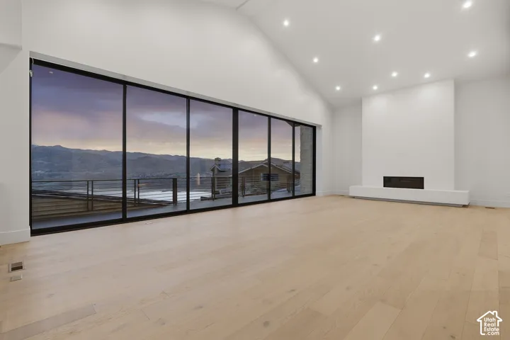 Vaulted ceiling, expansive multi-panel sliding glass wall, recessed lighting, wood-finish flooring, and built-in linear fireplace