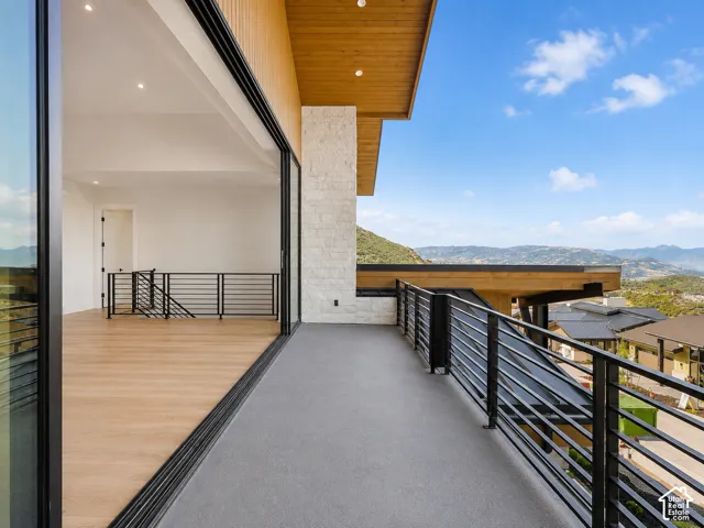 Expansive outdoor balcony with mountain scenery, featuring a stone accent wall, wood-finish ceiling, and modern horizontal railings