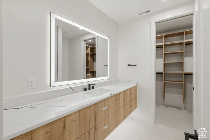 Floating vanity featuring light wood-finish cabinetry, white stone-patterned countertop with integrated sinks, matte black widespread faucets, and a large backlit rectangular mirror