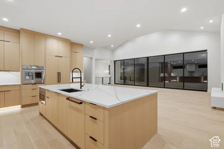 Kitchen featuring light wood-finish cabinetry, a large central island with quartz countertop, integrated stainless steel appliances, matte black hardware, and floor-to-ceiling multi-panel glass doors