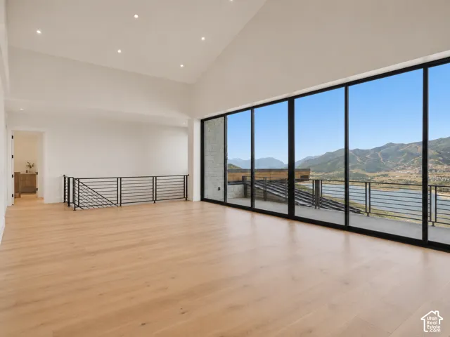 Vaulted ceilings with recessed lighting, expansive floor-to-ceiling windows, wood-finish flooring, and a black metal railing