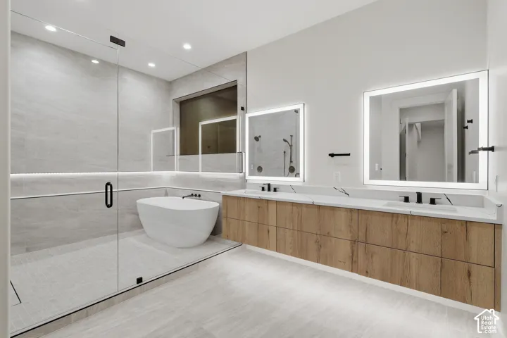 Floating wood-finish double vanity with stone countertop, undermount sinks, matte black fixtures, and integrated LED-lit mirrors, featuring a glass-enclosed wet room with a freestanding soaking tub and large-format tile wall surround