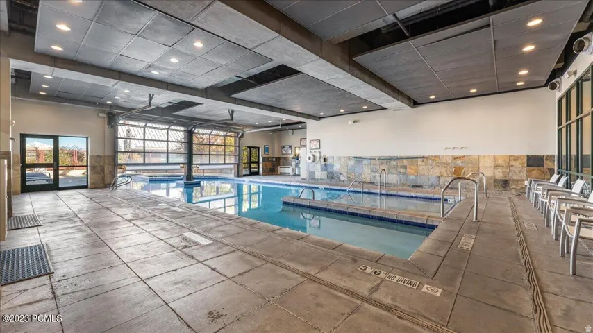 Indoor swimming pool with an integrated hot tub, framed by large glass roll-up doors and a stone accent wall