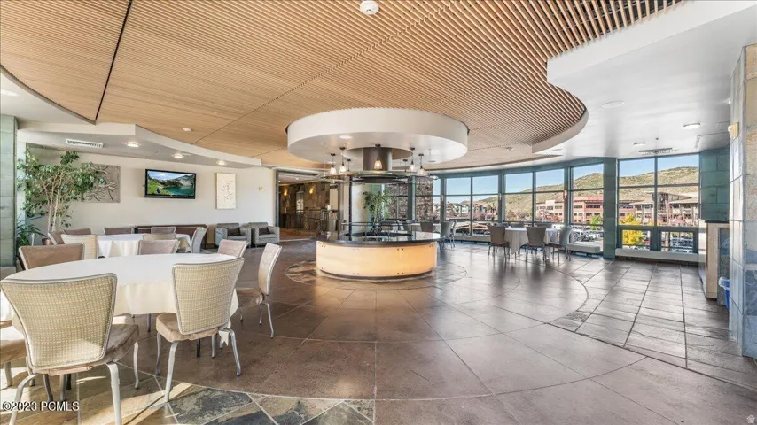 Expansive common area featuring a wood-panel ceiling, curved window wall, stone tile flooring, and a central circular reception desk