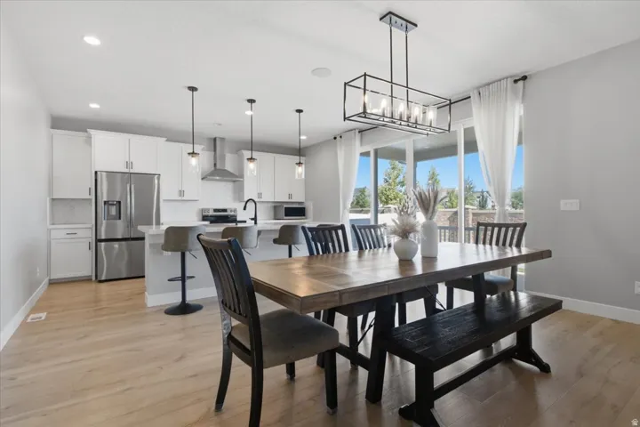 Open-concept kitchen and dining area featuring light wood-finish flooring, a contemporary linear chandelier, and white cabinetry