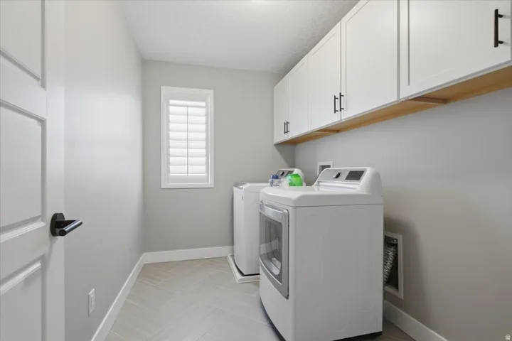 White shaker cabinetry with black hardware, wood-finish shelving, herringbone-patterned flooring, and a window with plantation shutters