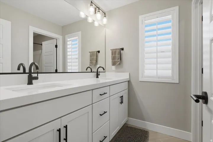 Dual vanity with integrated sinks, white cabinetry, matte black hardware, and a large wall-mounted mirror