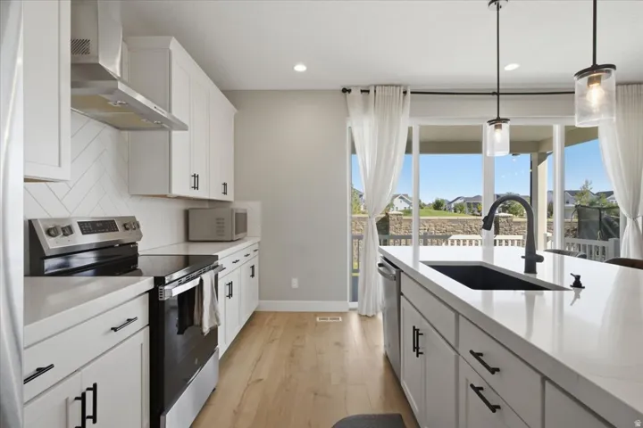 White cabinetry, herringbone tile backsplash, stainless steel appliances, center island with sink, and sliding glass doors