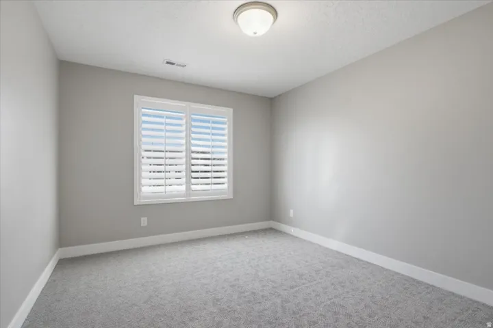 Recessed window with plantation shutters, neutral-toned walls, and soft gray carpeting