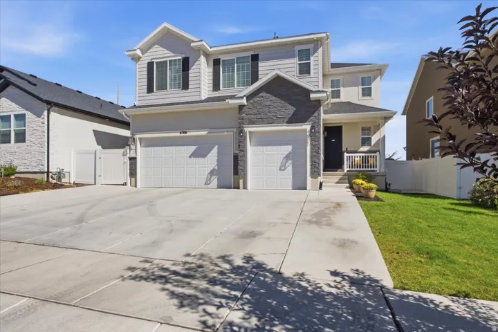 Two-story exterior with light gray siding and stone accents, featuring a two-car garage, a covered front porch, and a concrete driveway