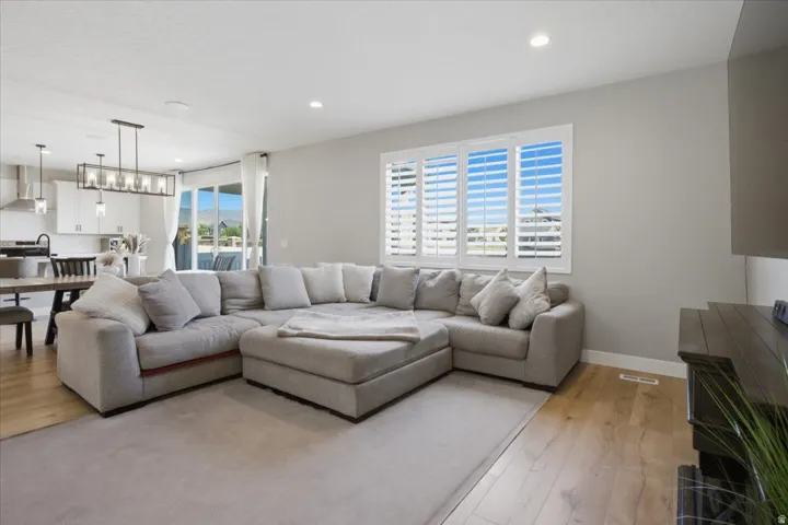 Open concept living space with wood-finish flooring, recessed lighting, and a large window featuring plantation shutters