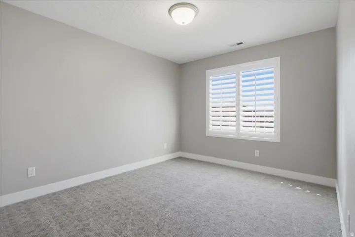 Neutral wall color, window with white plantation shutters, white trim, gray patterned carpeting, and a ceiling-mounted light fixture