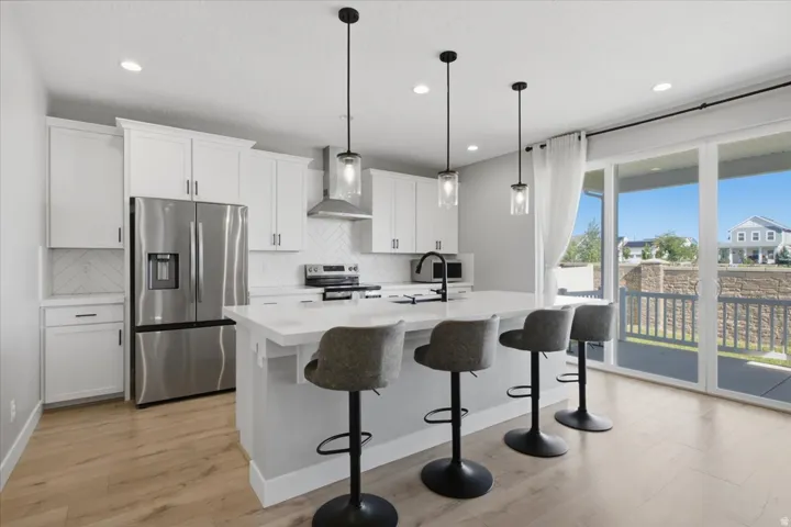 White cabinetry, stainless steel appliances, herringbone tile backsplash, white countertops, and wood-finish flooring