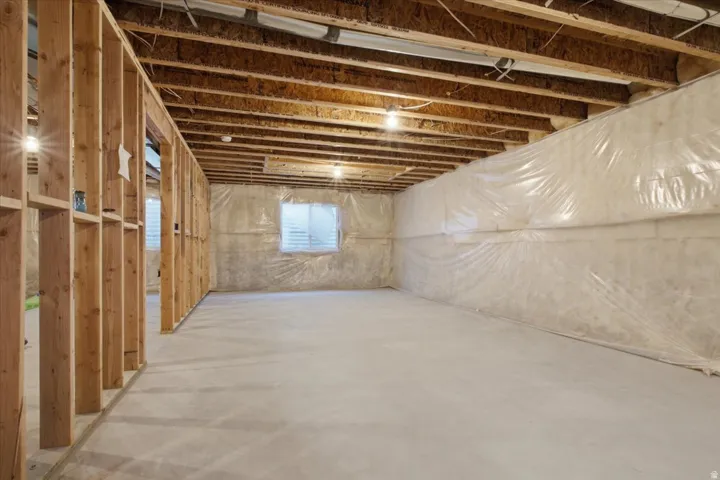 Unfinished lower level featuring wood framing, concrete flooring, exposed ceiling joists, and a window