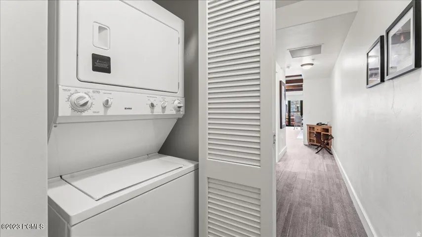 Dedicated laundry area with a stacked washer and dryer, adjacent to a hallway featuring wood-finish flooring and recessed lighting