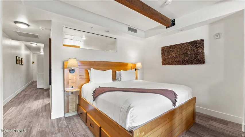 Wood-finish flooring, exposed ceiling beam, recessed lighting, and a built-in bed frame with integrated storage