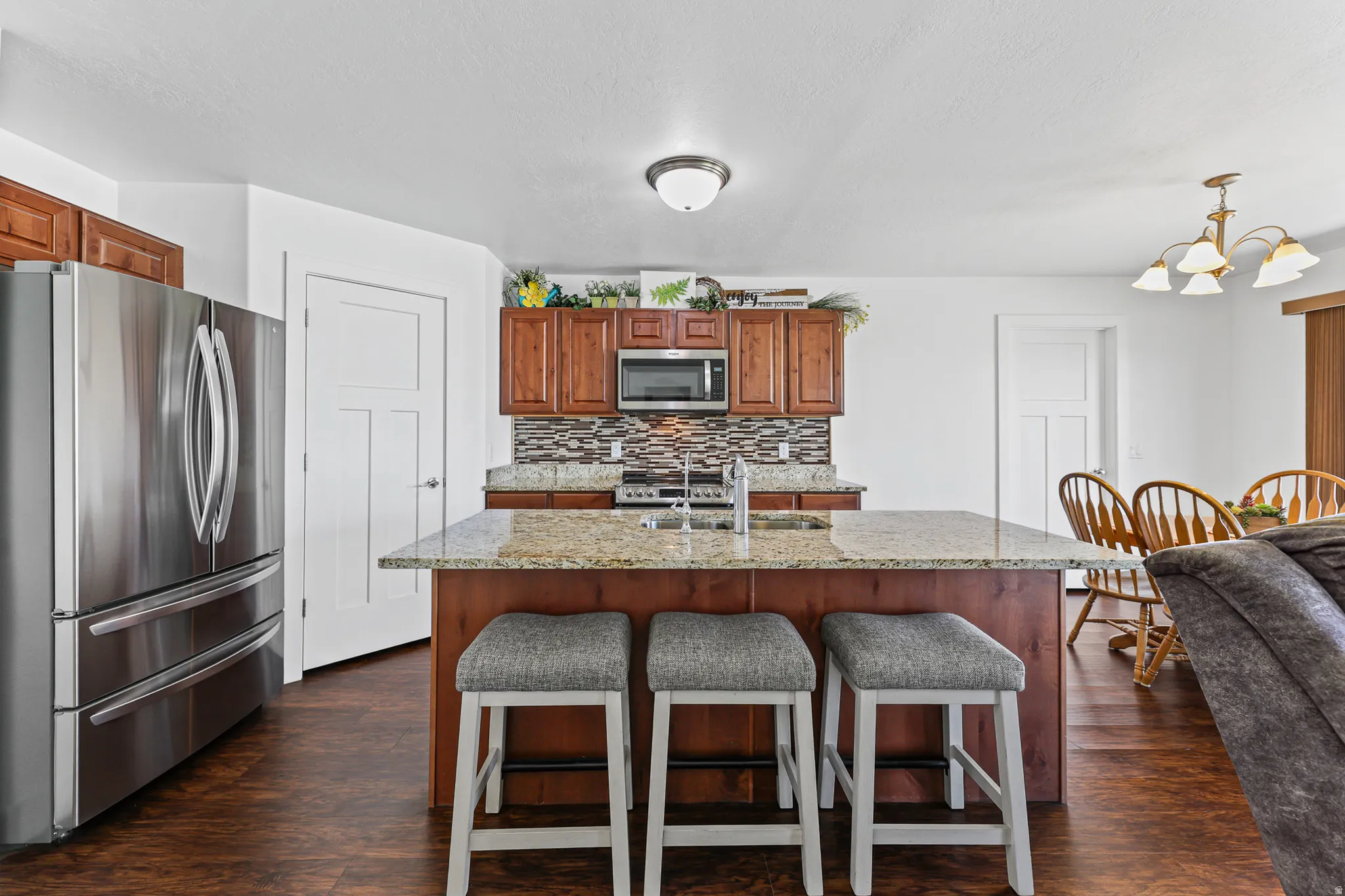 Spacious kitchen featuring an expansive center island with seating, stainless steel appliances, wood-finish cabinetry, and a mosaic tile backsplash
