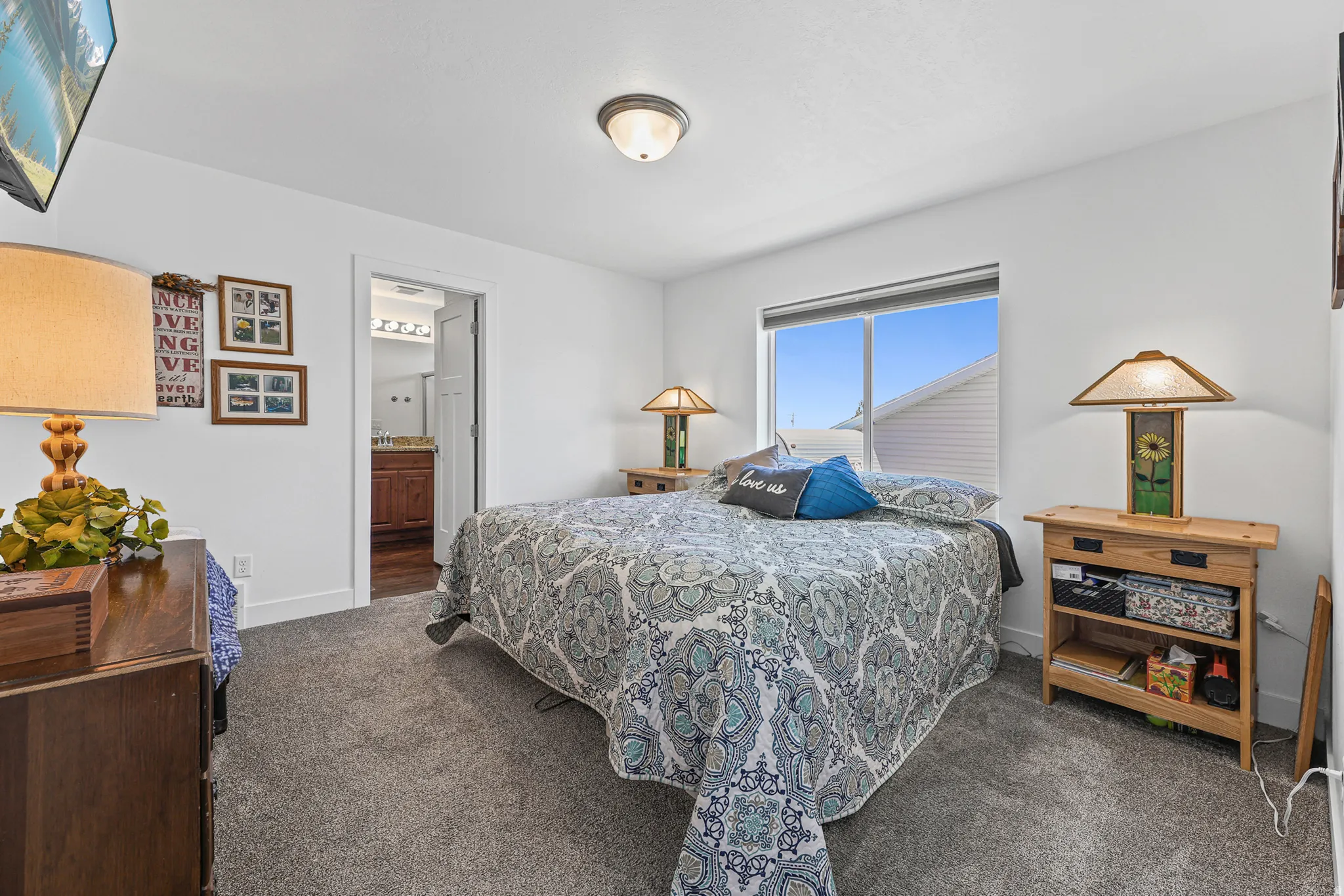 Neutral wall paint, carpet flooring, a large window, and an en-suite bathroom featuring a vanity with a countertop and built-in lighting