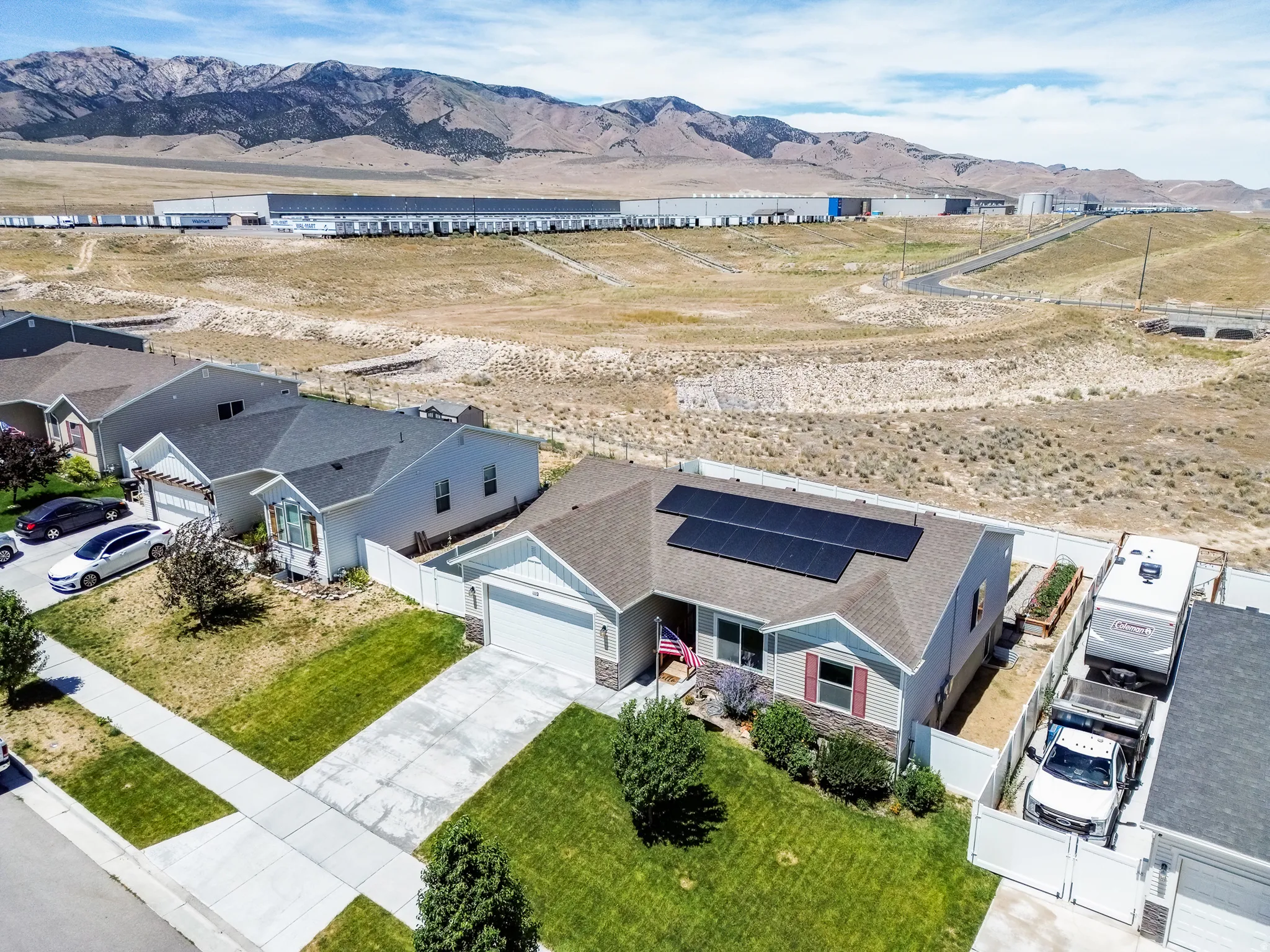Gray-sided residence with solar panels on the roof, an attached two-car garage, and a fenced yard