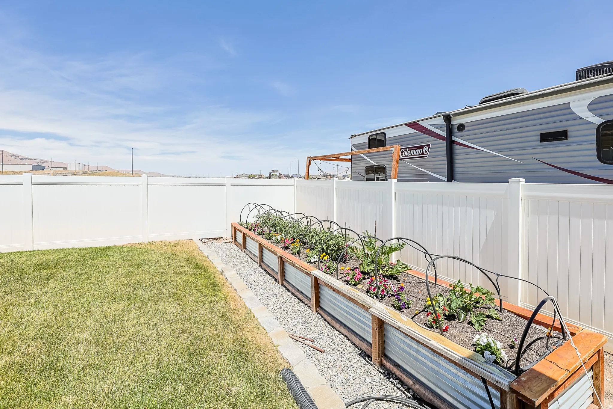 White privacy fencing encloses a manicured lawn and a raised garden bed with corrugated metal and wood-tone trim