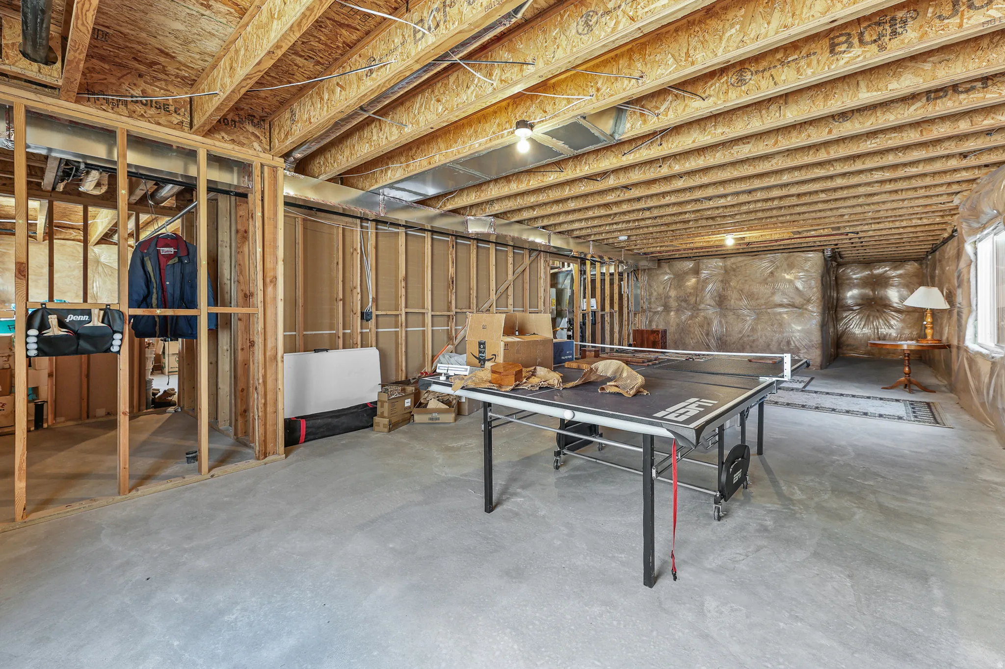 Unfinished basement with concrete flooring, exposed wood joists, and framed walls