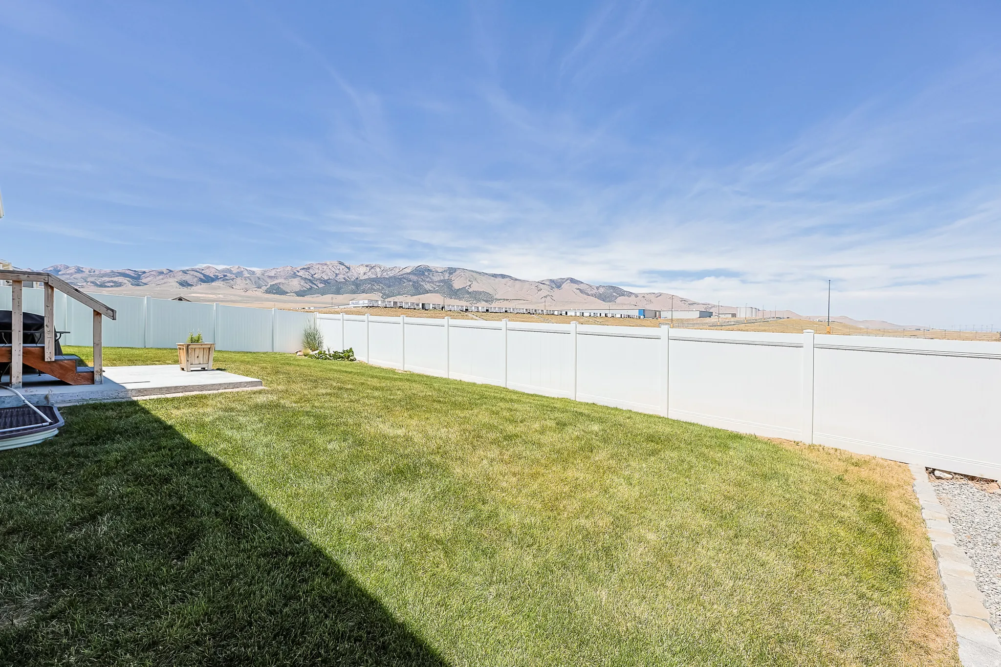 Expansive green lawn, white privacy fencing, concrete patio, elevated wooden deck, and distant mountain scenery