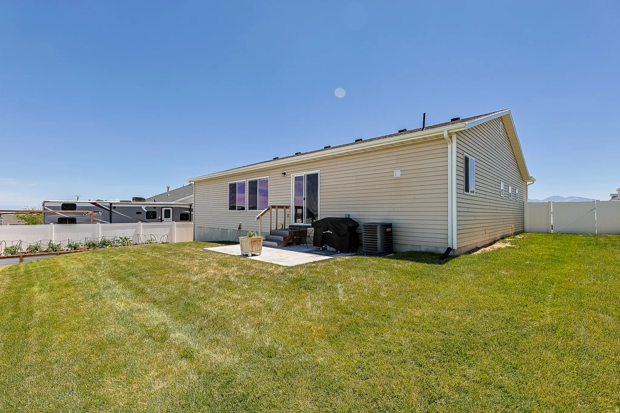 Expansive lawn area with a concrete patio, vinyl fencing, and a siding exterior