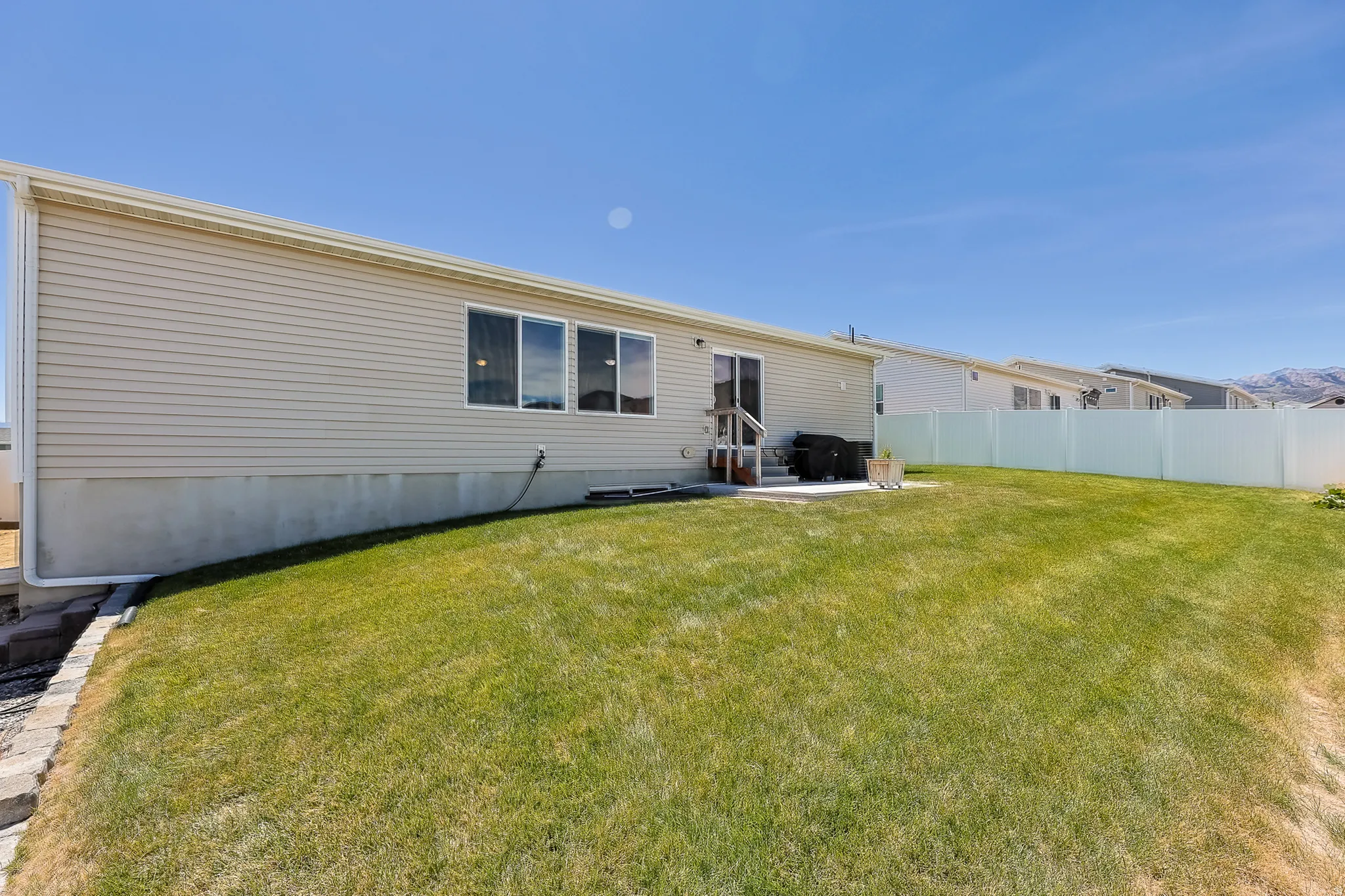 Expansive grassy yard featuring a concrete patio, sliding glass door access, and a vinyl privacy fence