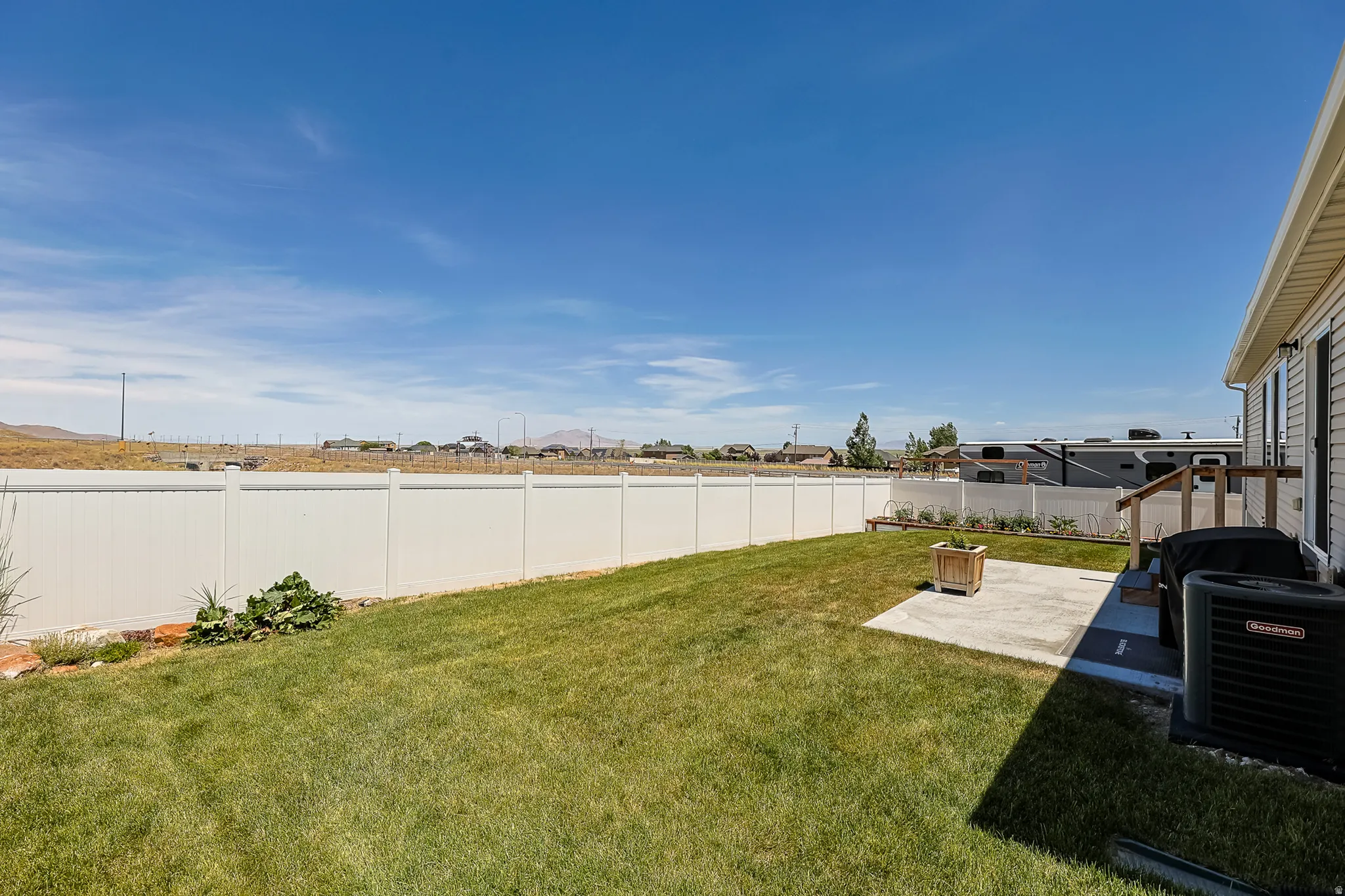 Expansive lawn area with a concrete patio, white privacy fencing, and wood deck access