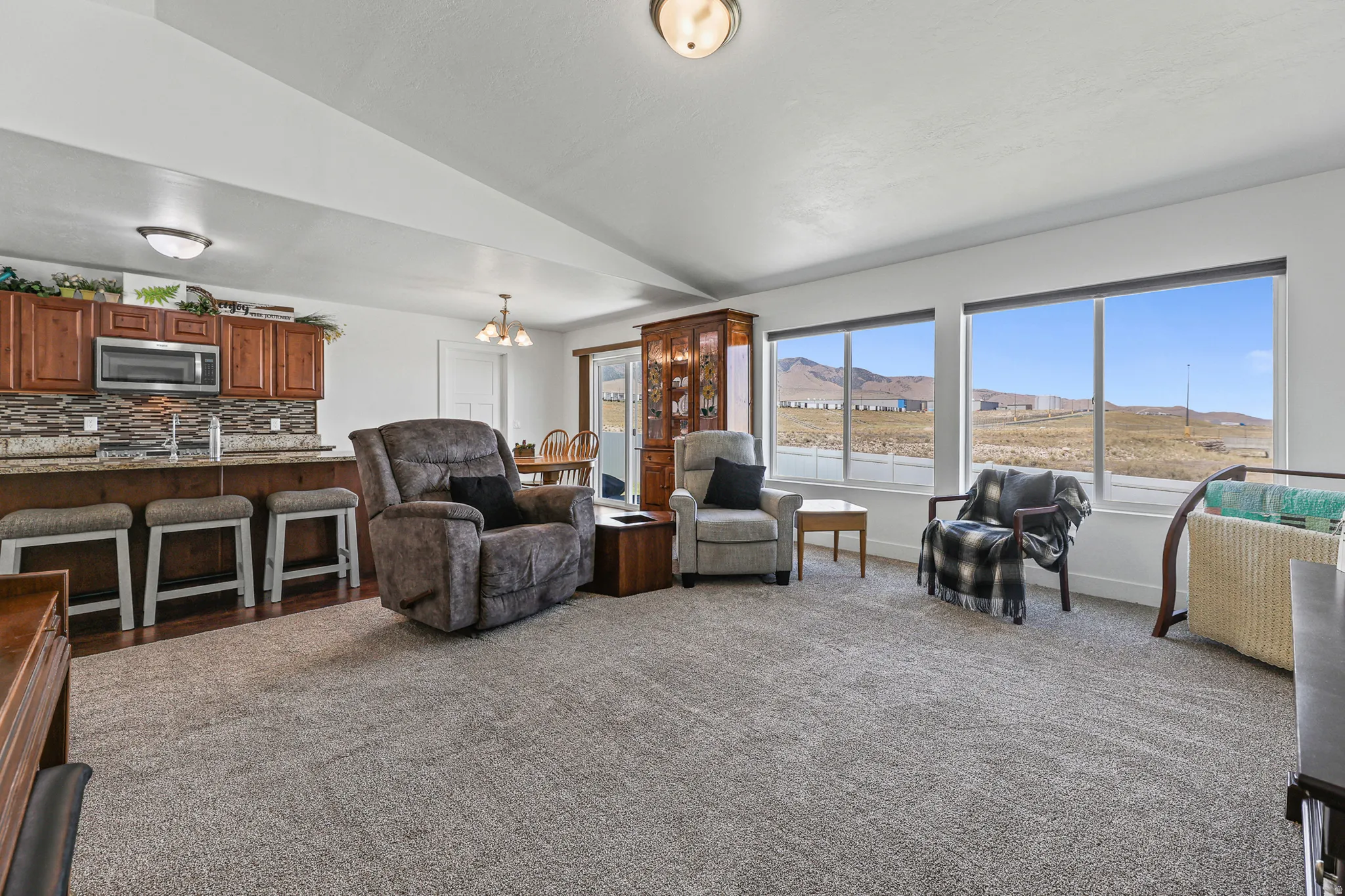 Open-concept living area featuring warm wood cabinetry, granite-style countertops, a tile backsplash, and expansive windows