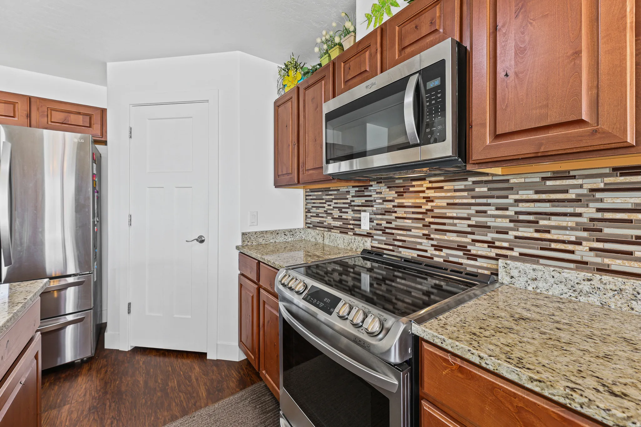 Stainless steel appliances, wood-finish flooring, granite countertops, tile backsplash, and wood cabinetry