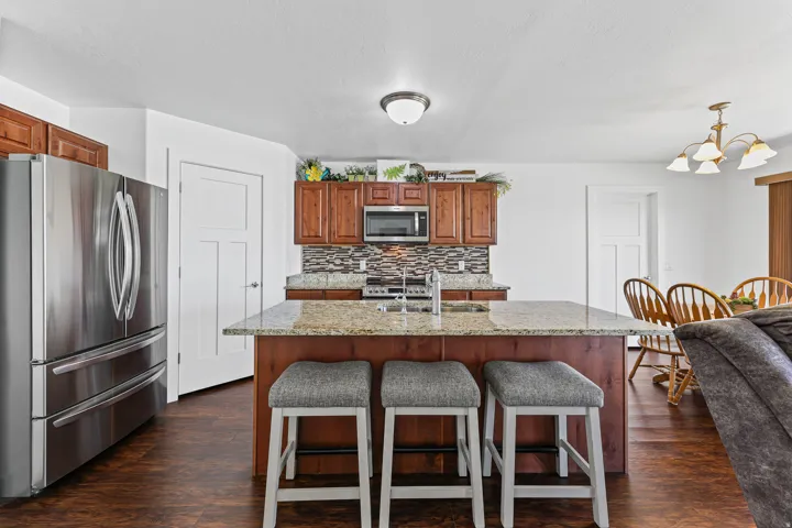 Spacious kitchen featuring an expansive center island with seating, stainless steel appliances, wood-finish cabinetry, and a mosaic tile backsplash