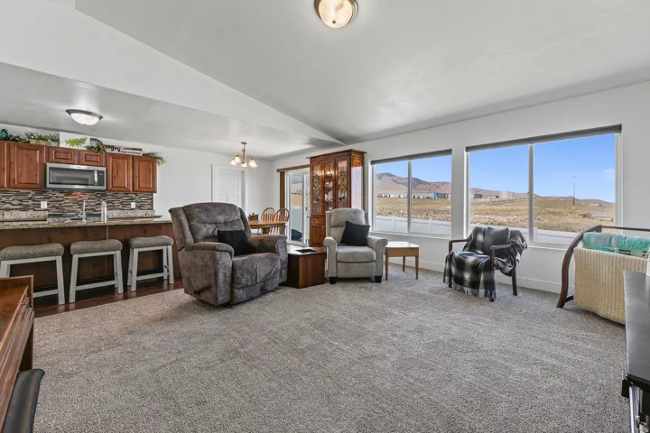 Open-concept living area featuring warm wood cabinetry, granite-style countertops, a tile backsplash, and expansive windows