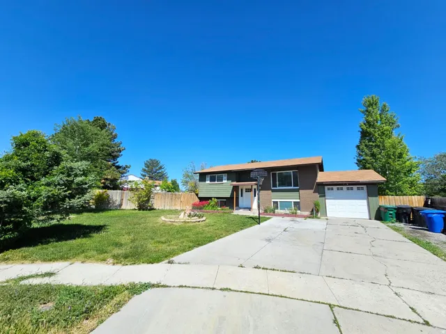 Split-level residence featuring a brown shingle roof, attached garage with white door, and a concrete driveway
