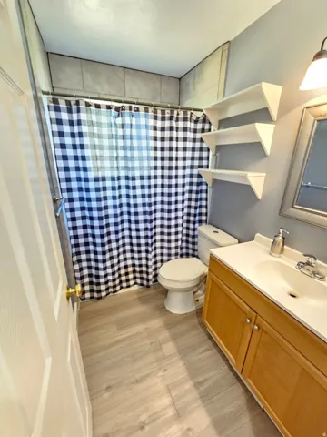 Bathroom featuring wood-finish flooring, a wood-finish vanity with white countertop, and a tiled shower surround
