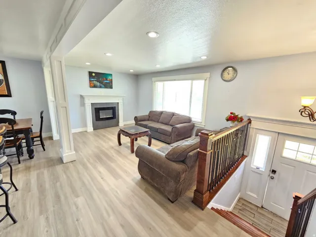 Living area with wood-finish flooring, a fireplace with a white mantel, and recessed lighting