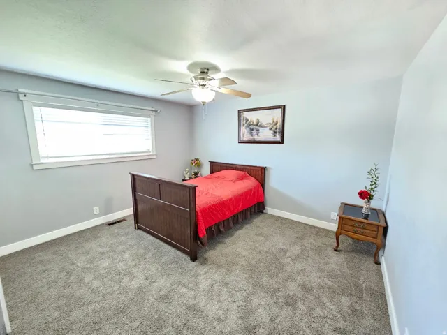 Light gray wall paint, gray carpeting, white window trim, and a ceiling fan with integrated lighting