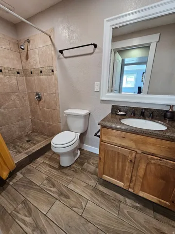 Walk-in shower with tiled surround and decorative accent band, wood-finish flooring, wood vanity cabinet with integrated sink, and framed mirror