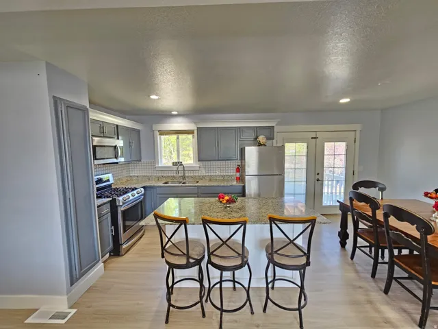 Kitchen featuring a center island with countertop seating, stainless steel appliances, grey cabinetry, and a tile backsplash