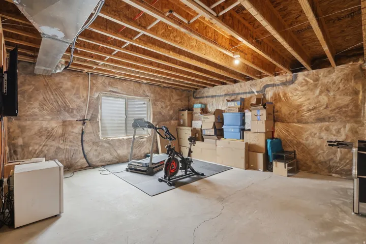 Unfinished basement featuring exposed wood joists, concrete flooring, and a window