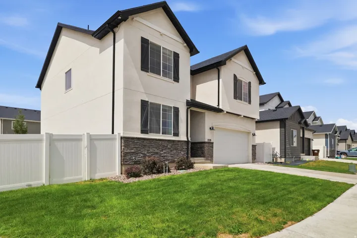 White stucco exterior with dark shutters, dark roof, and stone-clad foundation
